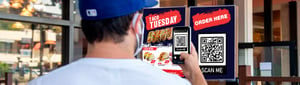 Man scanning QR code outside restaurant to order